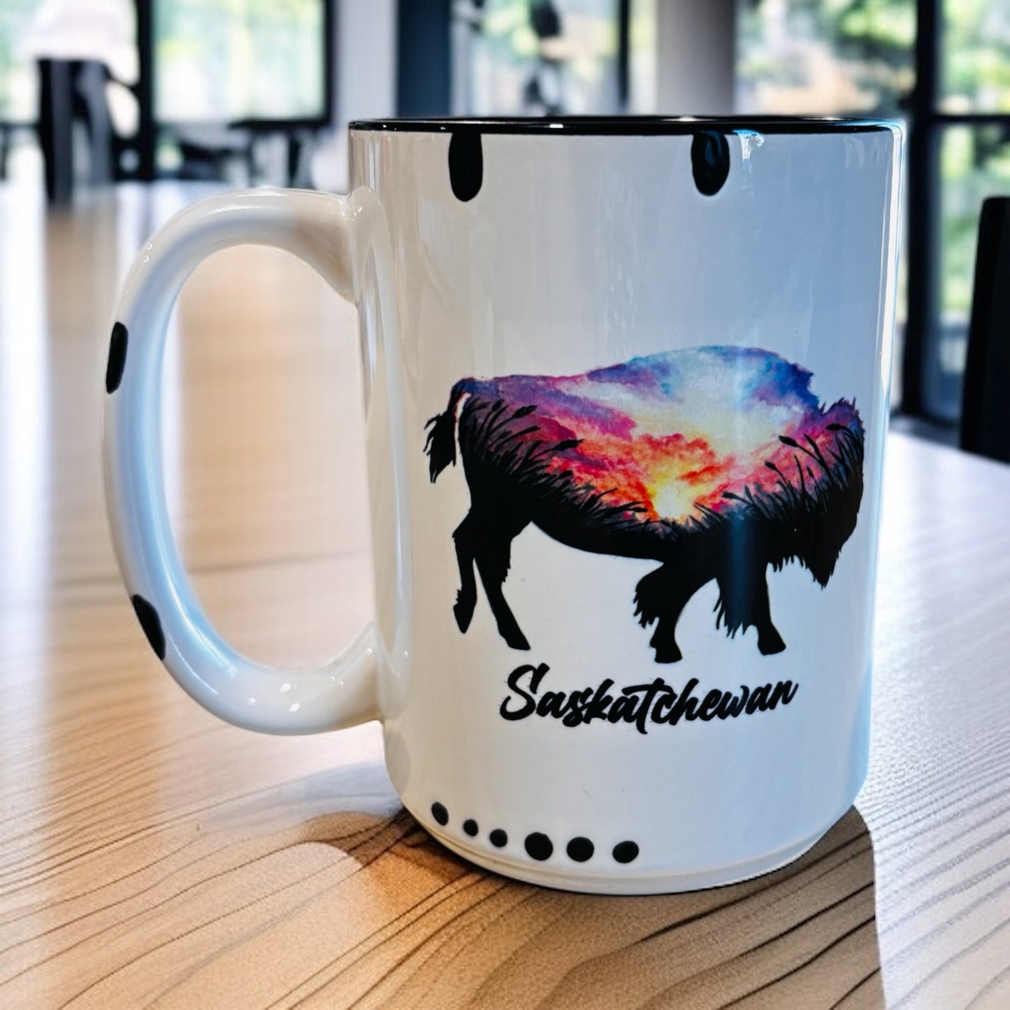 White mug with a colorful watercolor bison design and 'Saskatchewan' text sitting on a wooden surface.