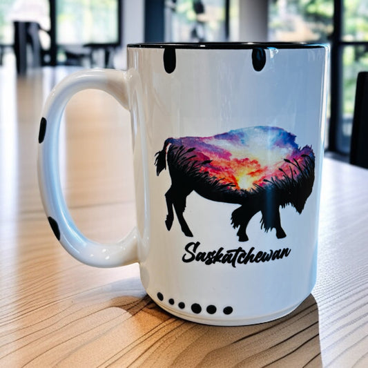 White mug with a colorful watercolor bison design and 'Saskatchewan' text sitting on a wooden surface.